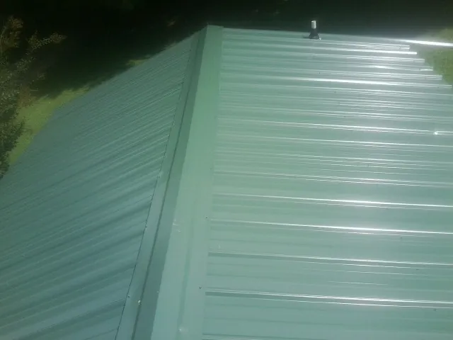 New green metal panels meeting at the ridge of a roof — Flat Roof Repair work by our crew in Bend