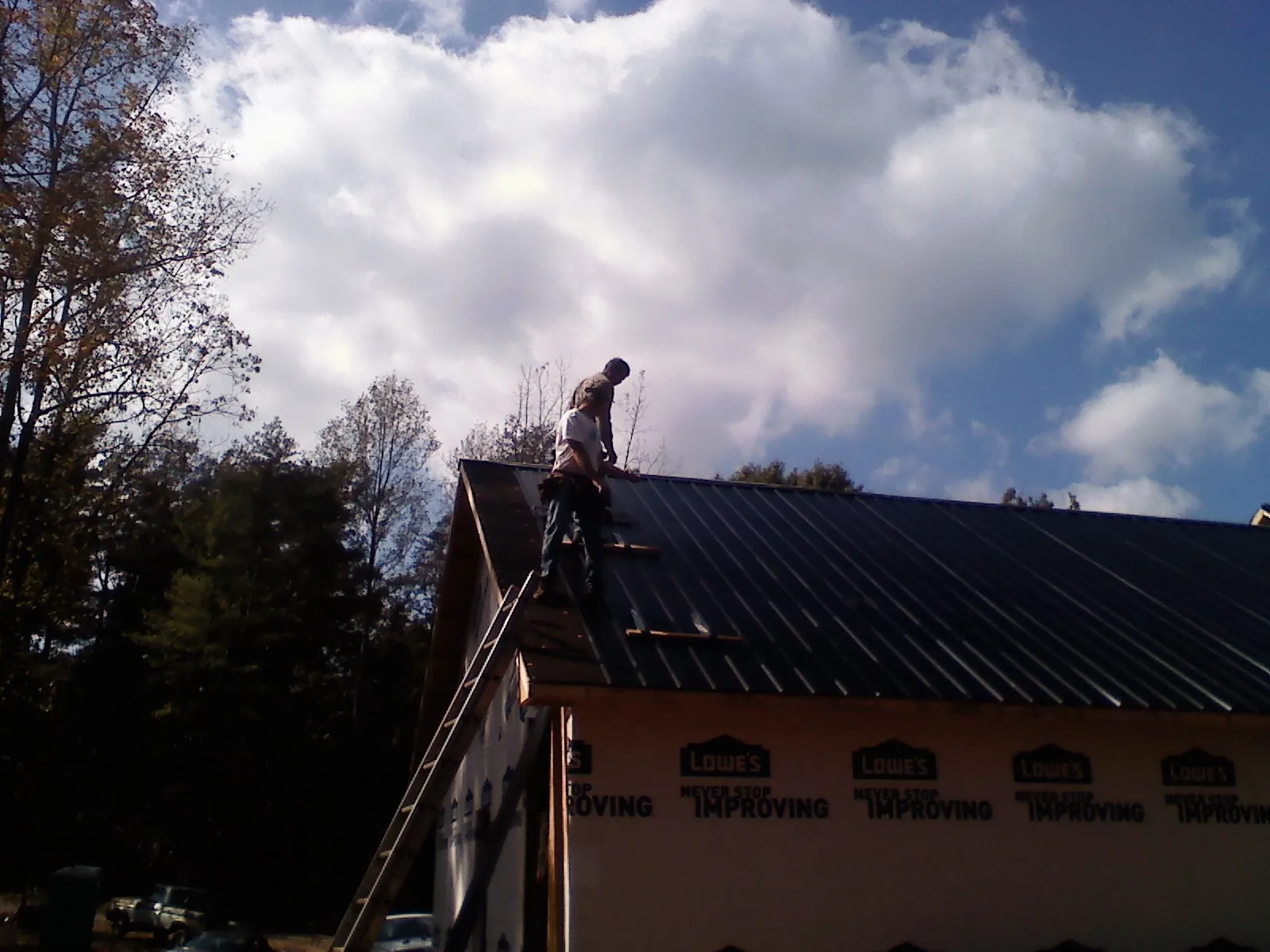 Roofer fastening dark metal panels high against a cloudy sky, from a Roof Inspection job in Bend